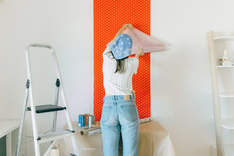 Back View of a Woman Putting Up a Wallpaper on the Wall